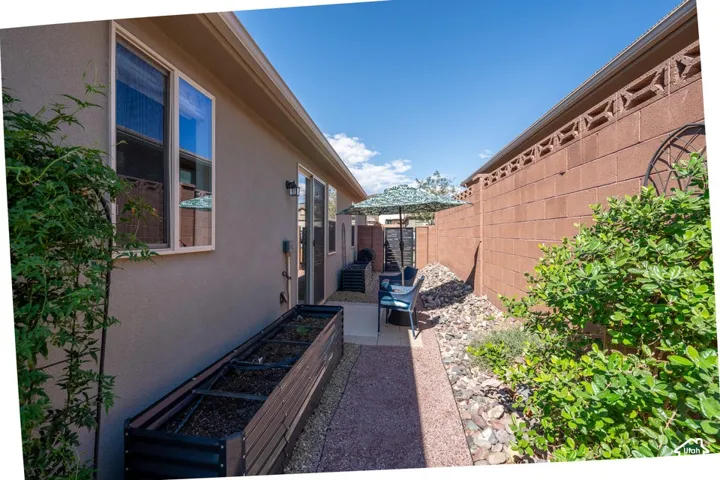 Side yard featuring a concrete patio, decorative rock landscaping, elevated metal garden planter, and a masonry perimeter wall with integrated breeze blocks