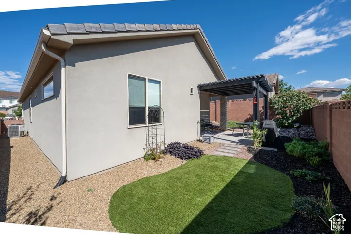 Stucco exterior featuring a covered pergola, concrete patio, synthetic turf area, and perimeter masonry fencing