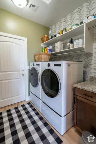Laundry area featuring patterned wall covering, built-in shelving, dark wood-finish cabinetry, and stone-finish countertop