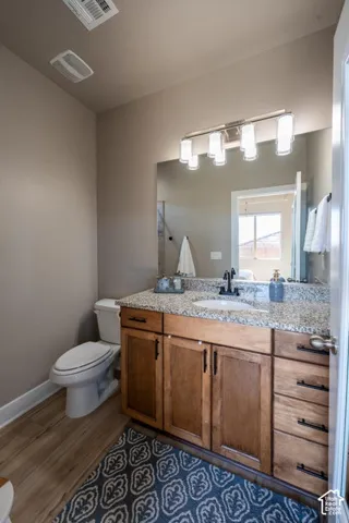 Vanity featuring wood cabinetry, stone-finish countertop, undermount sink, matte black faucet, and large wall-mounted mirror with multi-light fixture