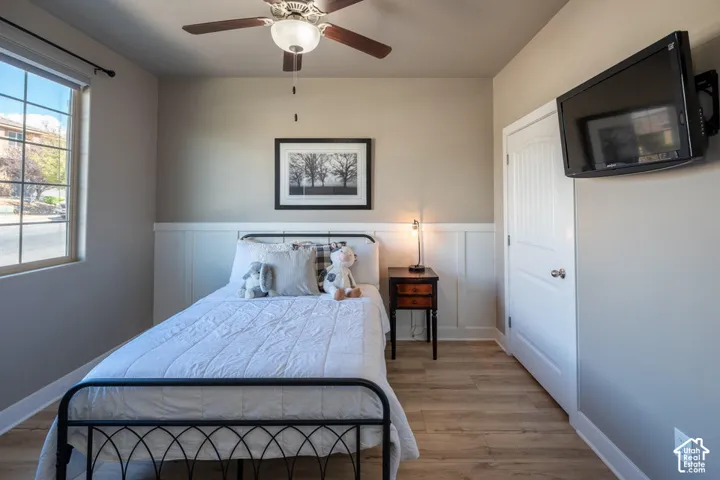 Wood-finish flooring, white board and batten wainscoting, grid-pattern window, and a ceiling fan with integrated lighting