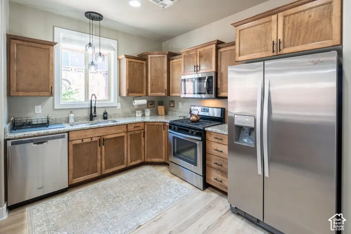 Kitchen featuring stained wood cabinetry, stone countertops, stainless steel appliances, a multi-light pendant fixture, and wood-finish flooring