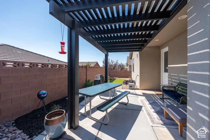 Covered patio featuring a black metal pergola, concrete flooring, and a decorative concrete block perimeter wall
