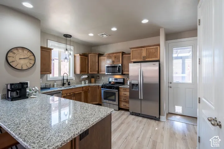 Kitchen featuring a stone-topped island, wood-finish cabinetry, stainless steel appliances, recessed lighting, and wood-finish flooring