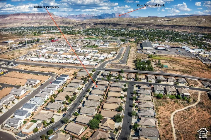 Aerial perspective of a residential neighborhood featuring paved streets, grid-patterned housing layouts, and distant mountain topography