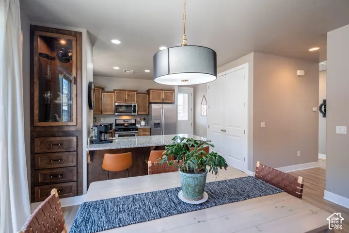 Kitchen featuring stained wood cabinetry, stone countertops, stainless steel appliances, a built-in glass-front display hutch, and a suspended drum pendant light