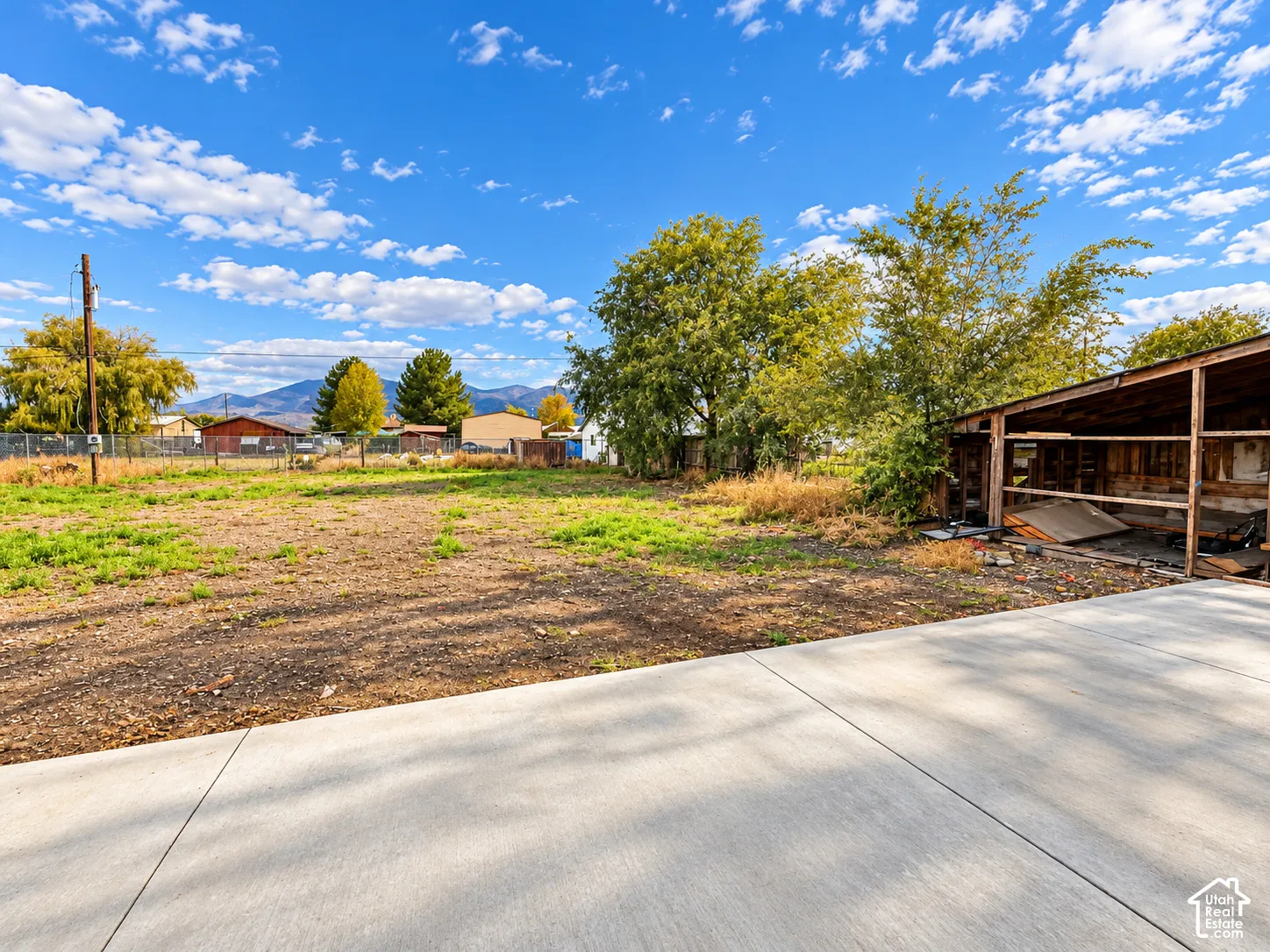 Expansive lot featuring a concrete pad, a wooden storage structure, mature trees, and mountain surroundings