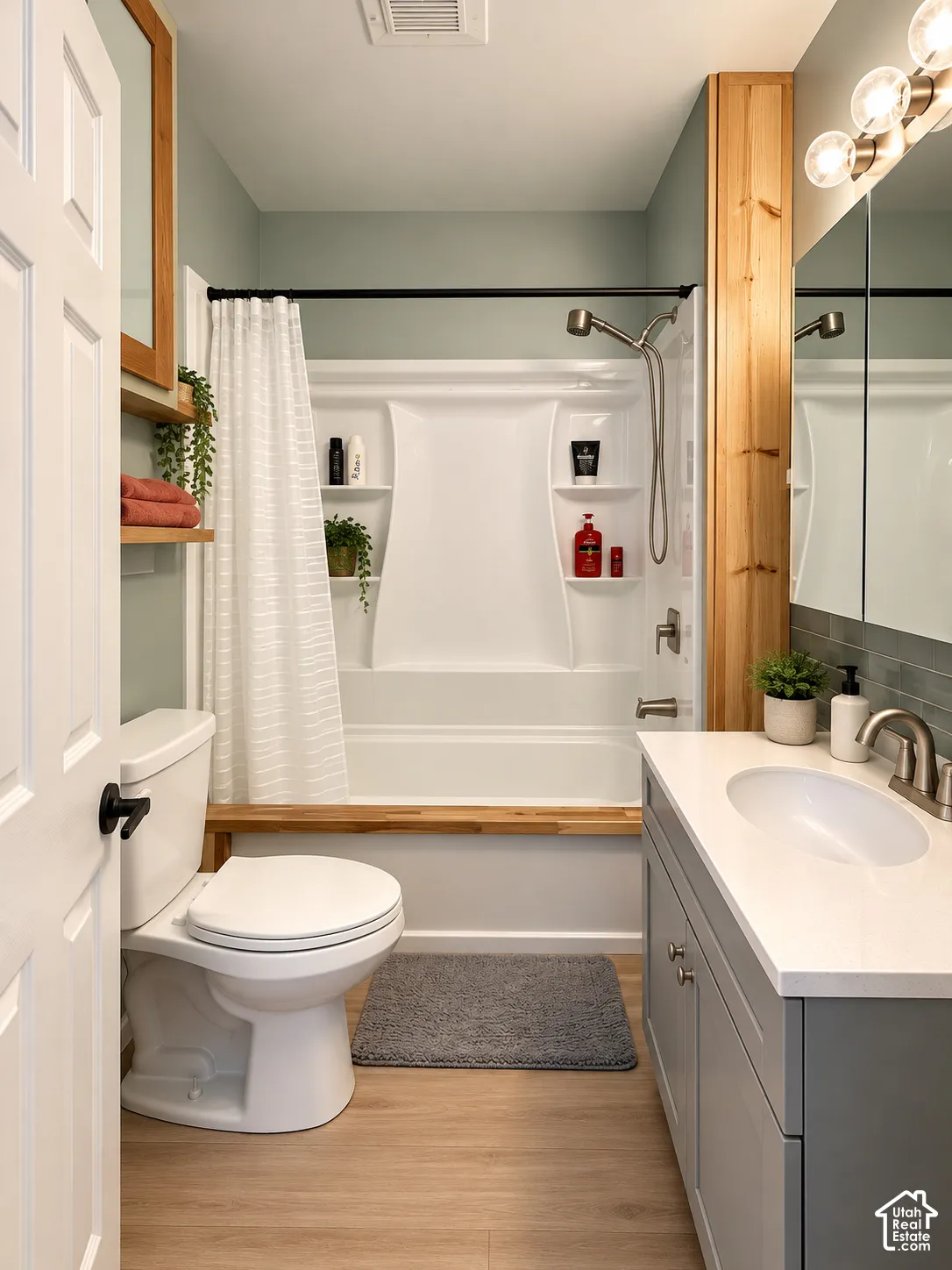 Bathroom featuring a vanity with a white countertop and undermount sink, built-in natural wood shelving, tub-shower combination with integrated shelving, wood-finish flooring, and a mirrored medicine cabinet