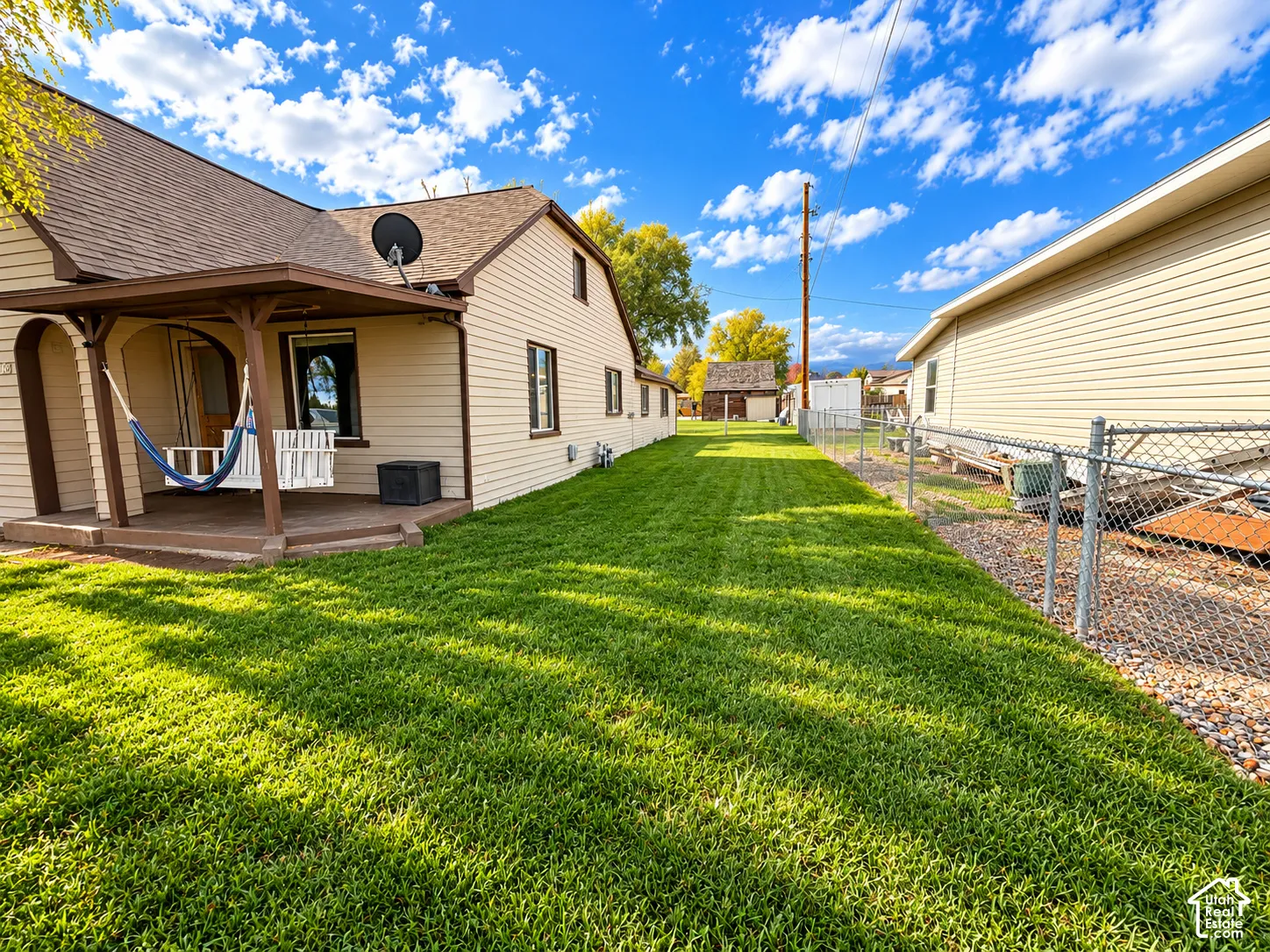 Covered porch featuring wood decking and arched supports, expansive lawn, and perimeter chain-link fencing