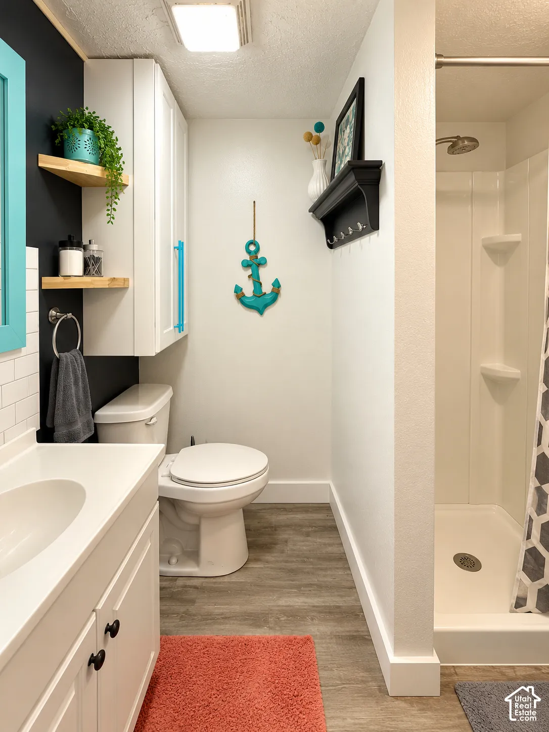 Bathroom featuring wood-finish flooring, white cabinetry with integrated shelving, a rectangular drop-in sink, and a walk-in shower stall with built-in soap ledges