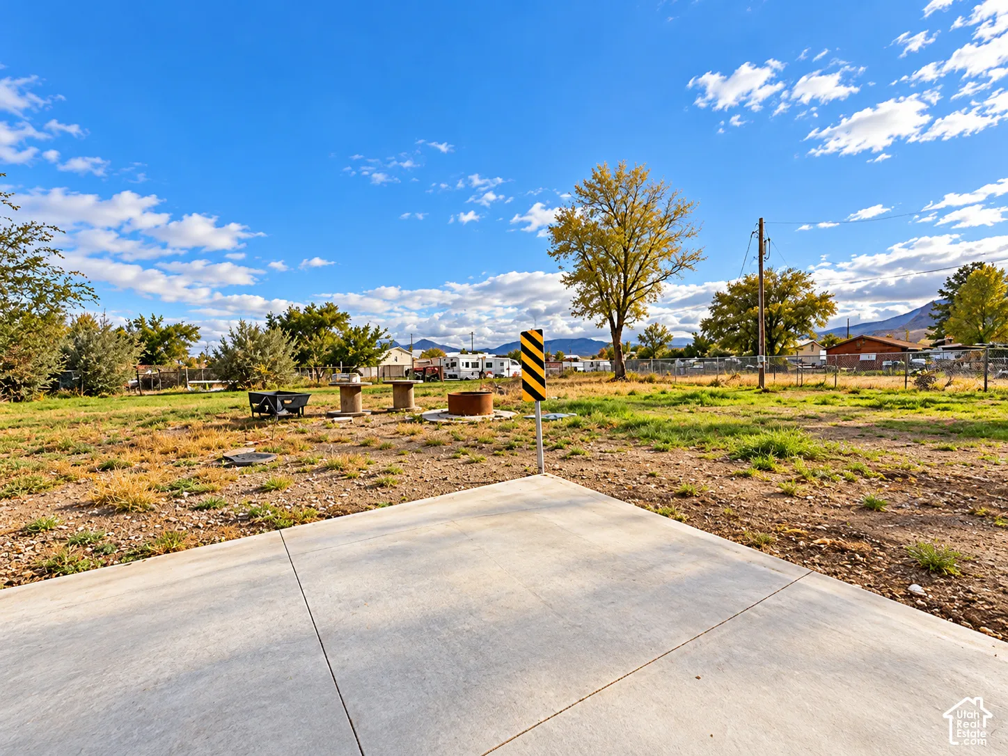 Expansive open lot featuring a concrete slab foundation, mountain backdrop, mature trees, and chain-link perimeter fencing