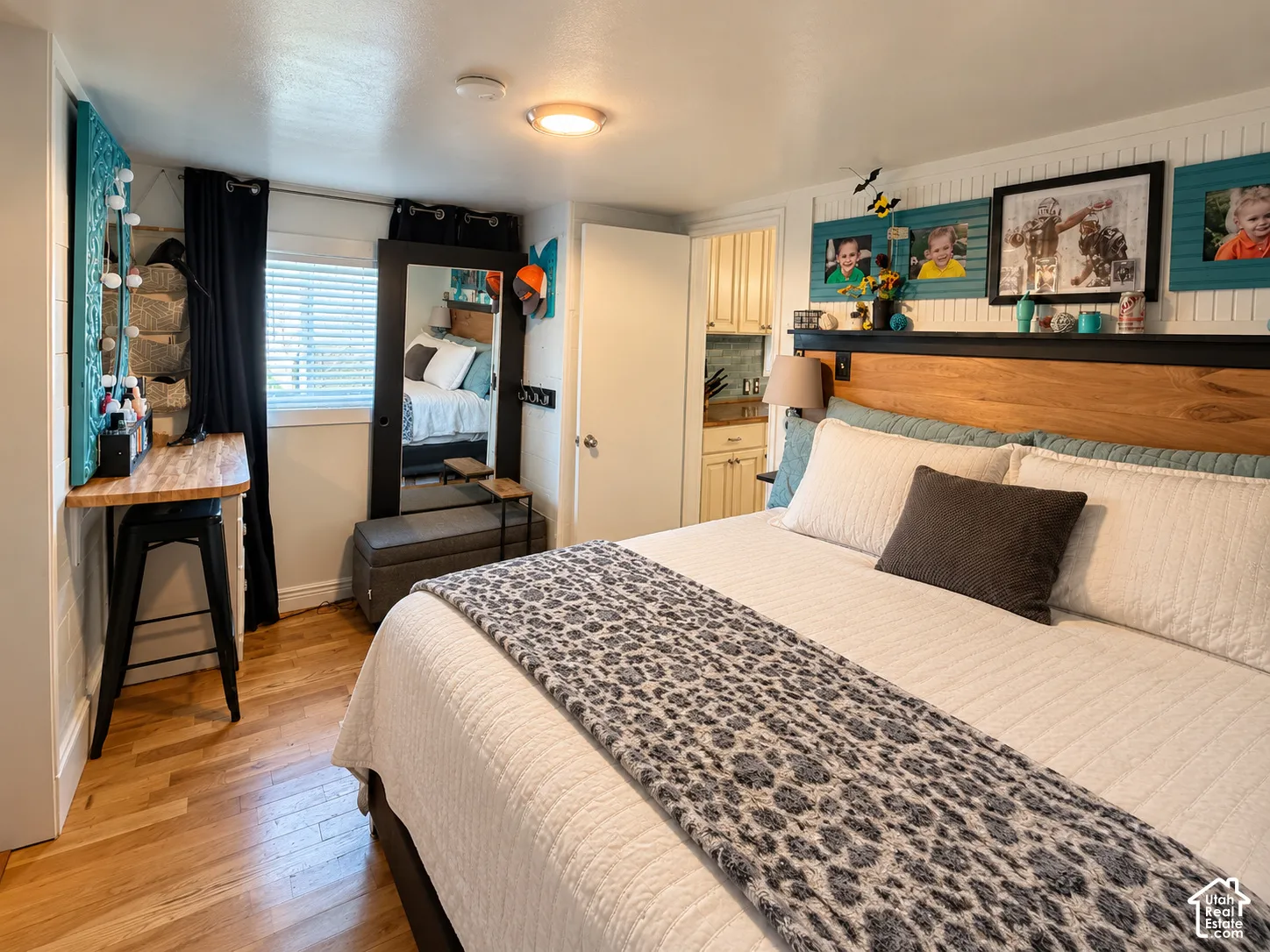 Bedroom interior featuring wood-finish flooring, beadboard wall paneling, built-in wooden headboard shelving, and a wall-mounted desk
