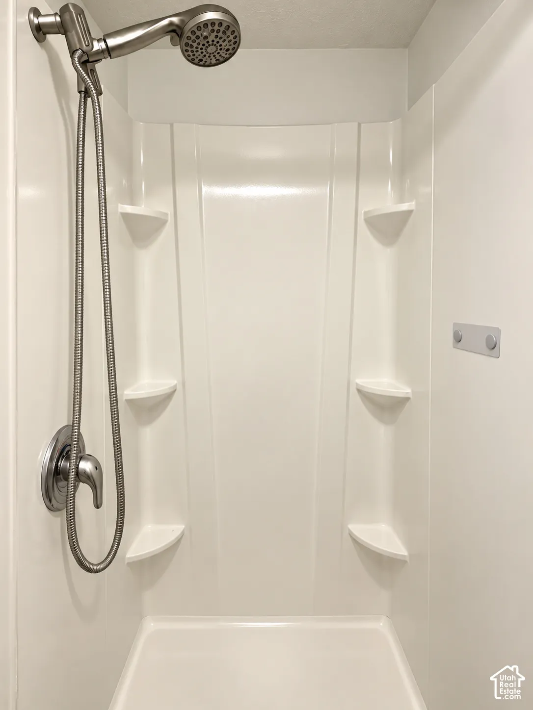 Shower stall featuring a molded surround with four built-in corner shelves, a brushed nickel single-handle mixing valve, and a coordinating hand-held shower head on a flexible hose