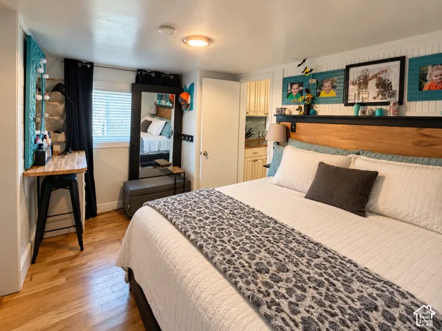 Bedroom interior featuring wood-finish flooring, beadboard wall paneling, built-in wooden headboard shelving, and a wall-mounted desk