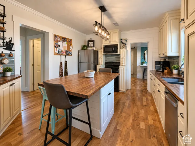 Kitchen featuring off-white cabinetry, wood-surface countertops, center island with shiplap detailing, stainless steel appliances, and multi-bulb pendant lighting