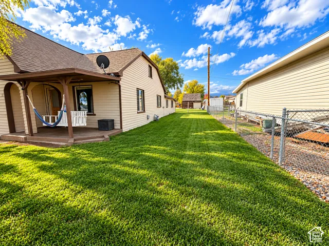 Covered porch featuring wood decking and arched supports, expansive lawn, and perimeter chain-link fencing