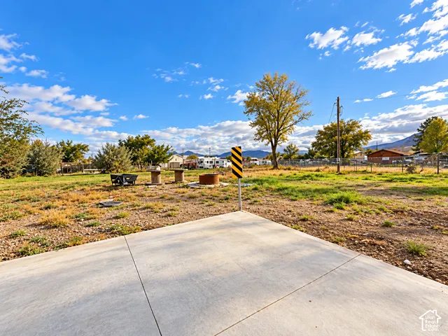 Expansive open lot featuring a concrete slab foundation, mountain backdrop, mature trees, and chain-link perimeter fencing