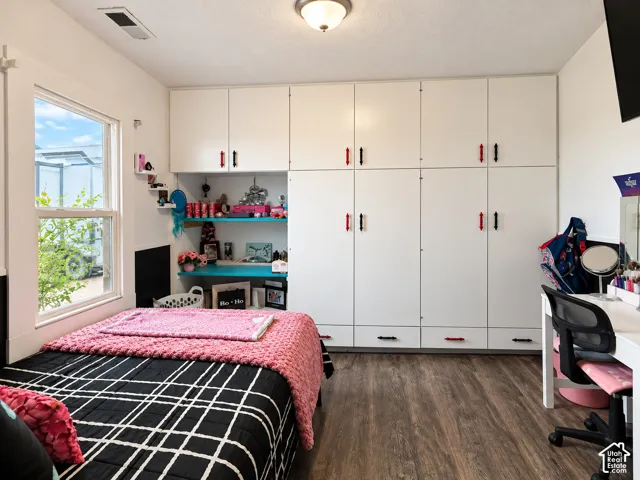 Wall-to-wall built-in cabinetry featuring white doors with dual-tone hardware, integrated desk space with open shelving, wood-finish flooring, and a single-hung window