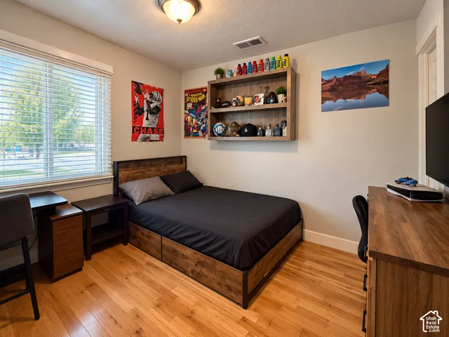 Bedroom featuring wood-finish flooring, a large window with horizontal blinds, and wall-mounted shelving