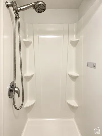 Shower stall featuring a molded surround with four built-in corner shelves, a brushed nickel single-handle mixing valve, and a coordinating hand-held shower head on a flexible hose