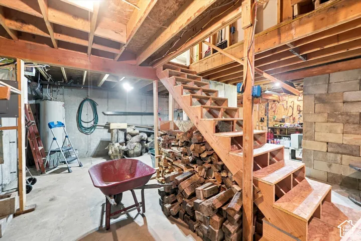 Unfinished basement featuring concrete flooring, exposed wood ceiling joists, concrete masonry unit walls, and an open wood staircase