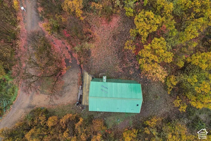 Aerial perspective of a property featuring a green metal roof, exterior chimney, and a wooden deck situated on a lot with mature trees
