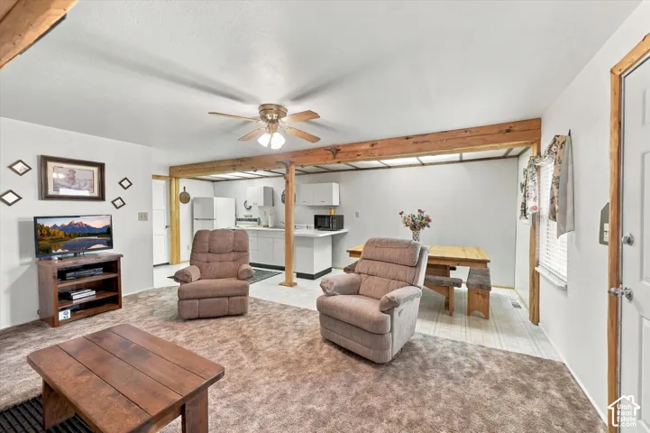 Open-concept living space featuring exposed wooden structural beams, a central ceiling fan, and carpeted flooring