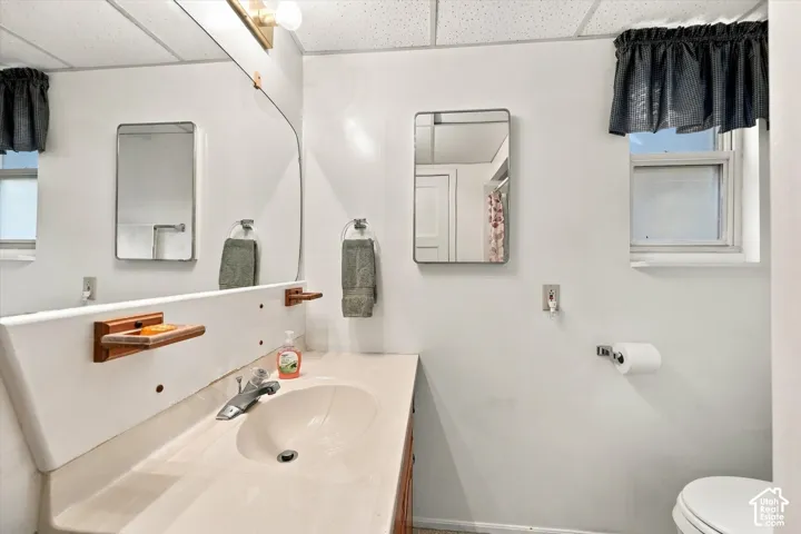 Bathroom featuring a molded sink and countertop unit, expansive wall-mounted mirror, metal faucet hardware, and two windows