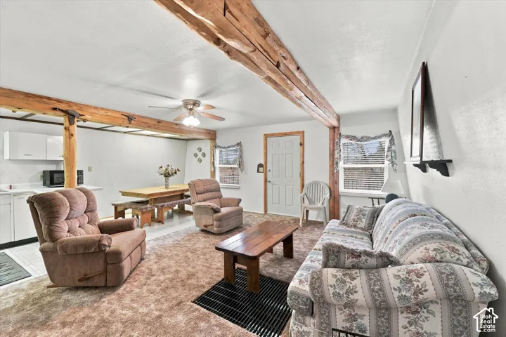Exposed timber ceiling beams, white cabinetry, integrated ceiling fan, and window-lined walls