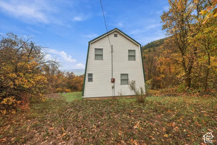 A-frame structure featuring light-colored siding, dark-trimmed rooflines, and multiple double-hung windows, situated within a wooded lot