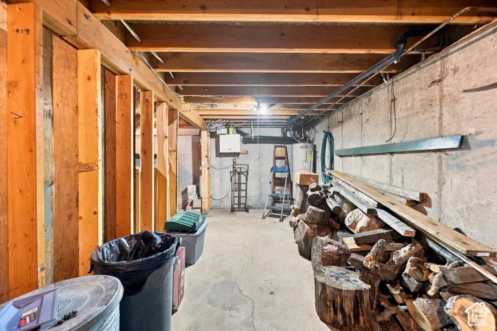 Unfinished basement area featuring exposed timber framing, concrete block walls, and concrete flooring