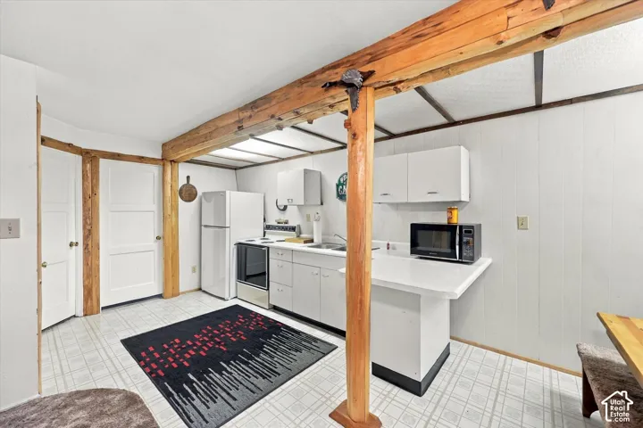 Kitchen featuring exposed wood structural beams, white cabinetry, solid-surface countertops, and tiled flooring