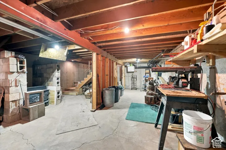 Unfinished basement featuring exposed wood-beam ceiling joists, concrete flooring, concrete masonry unit walls, and integrated wooden shelving