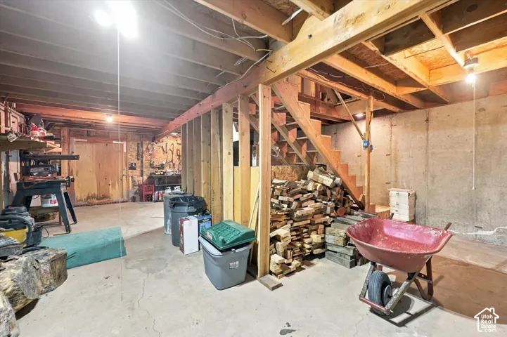 Unfinished basement featuring exposed wood joists, concrete foundation walls, a concrete floor, and an open wooden staircase