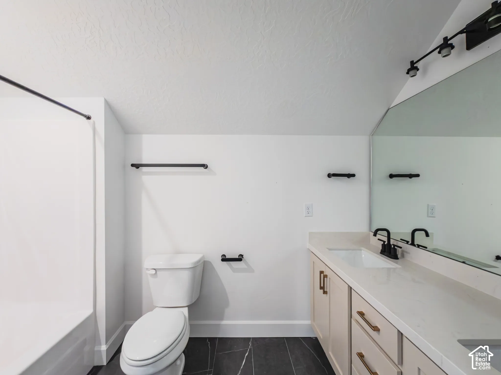 Vanity with stone countertop, dual undermount sinks, matte black fixtures, and large wall-mounted mirror, featuring dark tiled flooring and a shower-tub combination