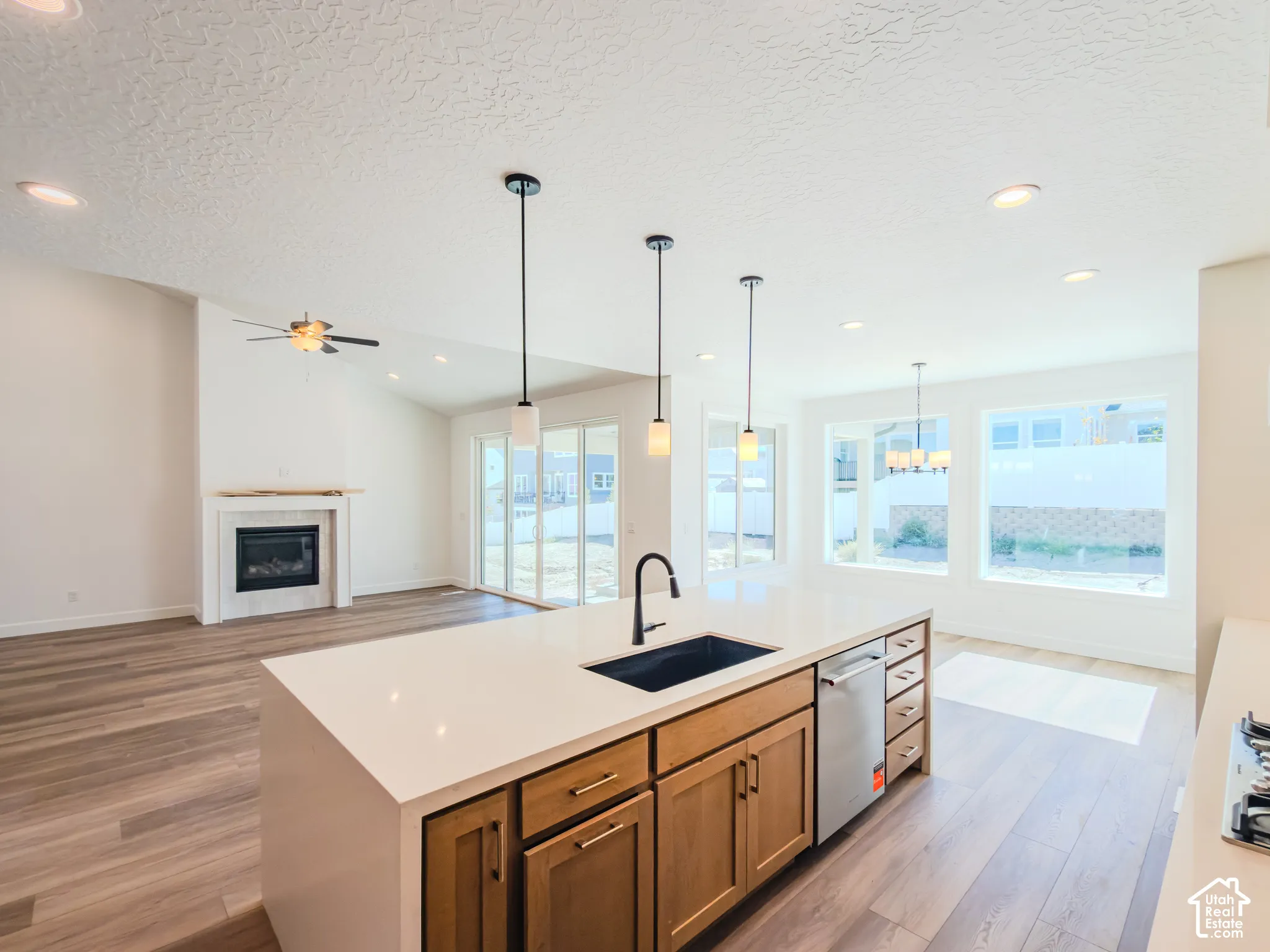 Kitchen island featuring a quartz countertop, under-mount sink, and matte black faucet, complemented by wood-finish cabinetry, recessed lighting, and pendant fixtures