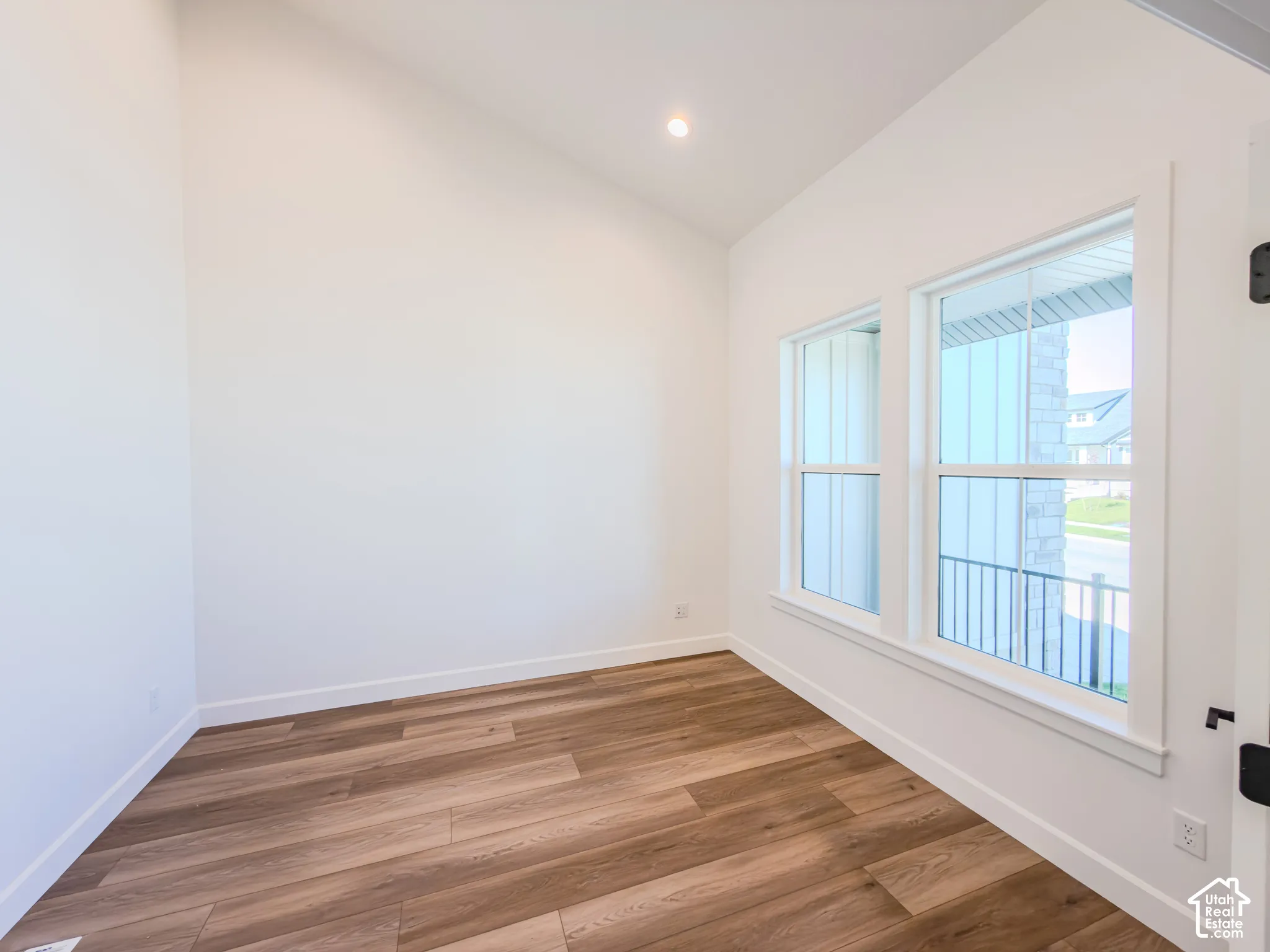 Vaulted ceiling room featuring wood-finish flooring, dual windows with grid detailing, and recessed lighting