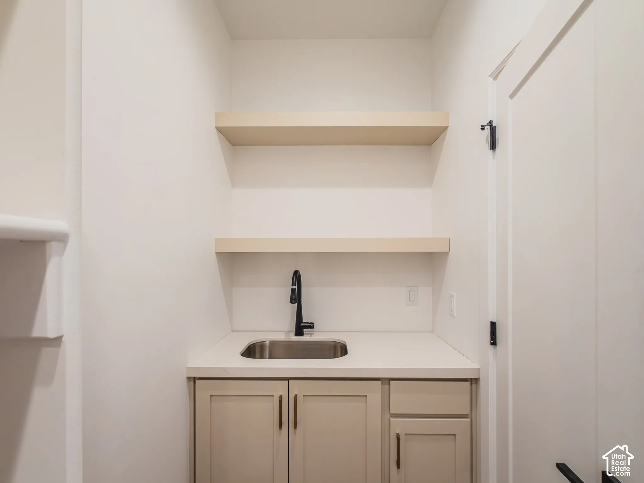 Built-in wet bar featuring custom cabinetry, solid-surface countertops, an undermount sink with a matte black faucet, and dual floating shelves