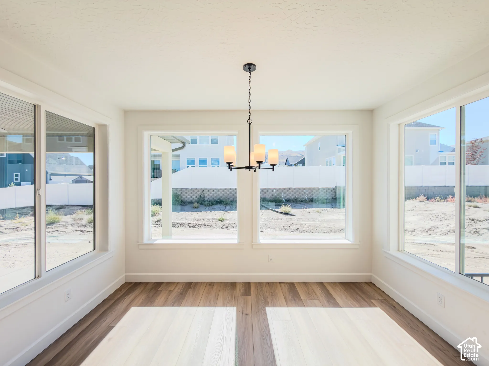 Expansive space featuring multiple oversized windows, wood-finish flooring, and a modern tiered chandelier with frosted glass shades