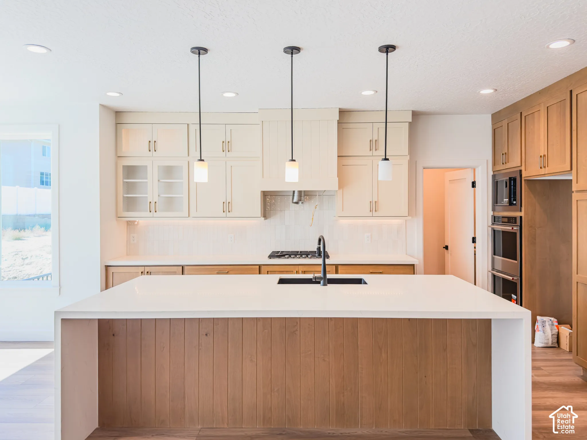 Kitchen featuring a large central island with waterfall-edge countertop, two-tone cabinetry, built-in double wall oven, gas cooktop, and three pendant light fixtures