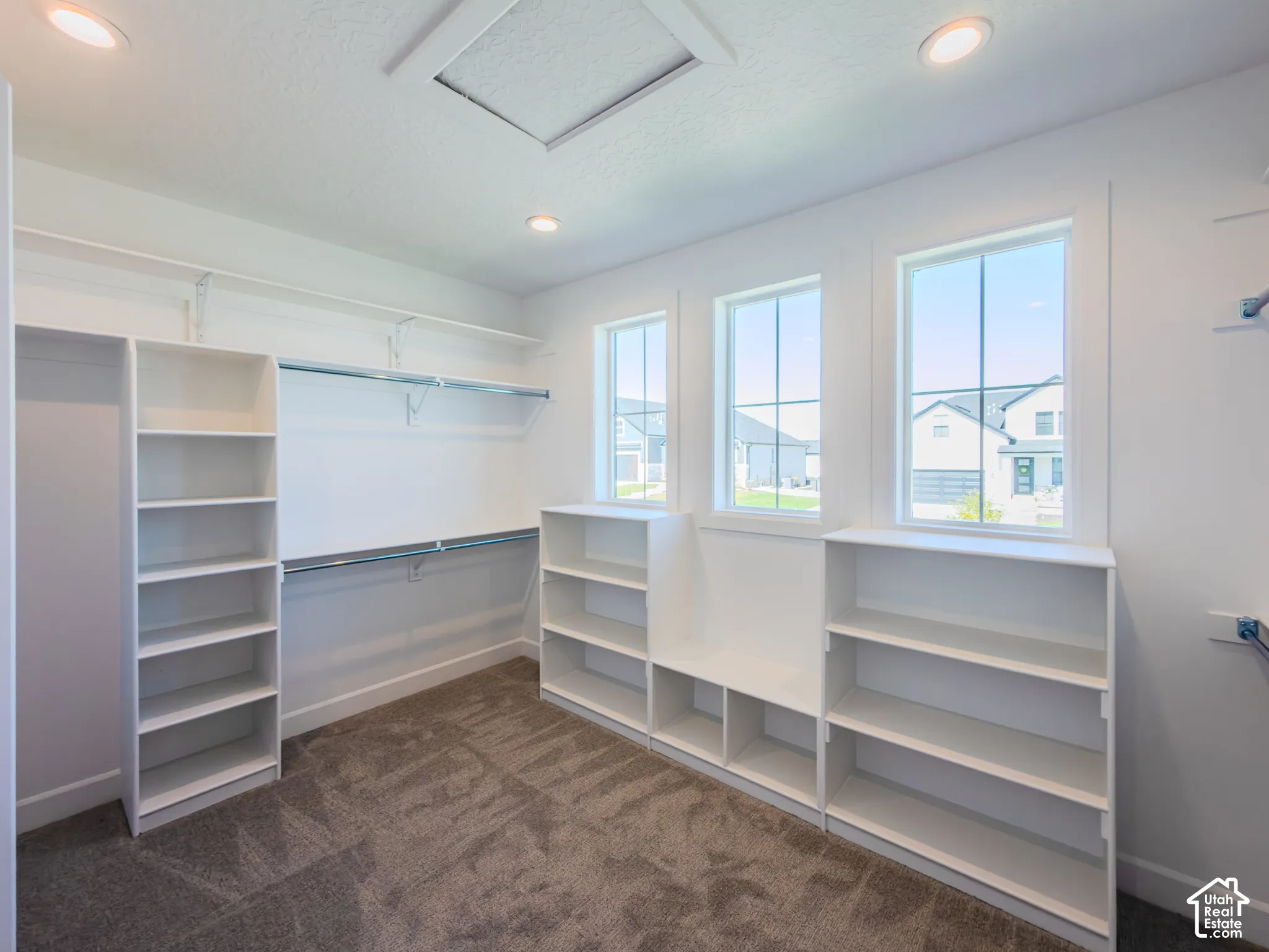 Walk-in closet featuring white built-in shelving, integrated hanging rods, three grid-pane windows, and recessed ceiling lighting