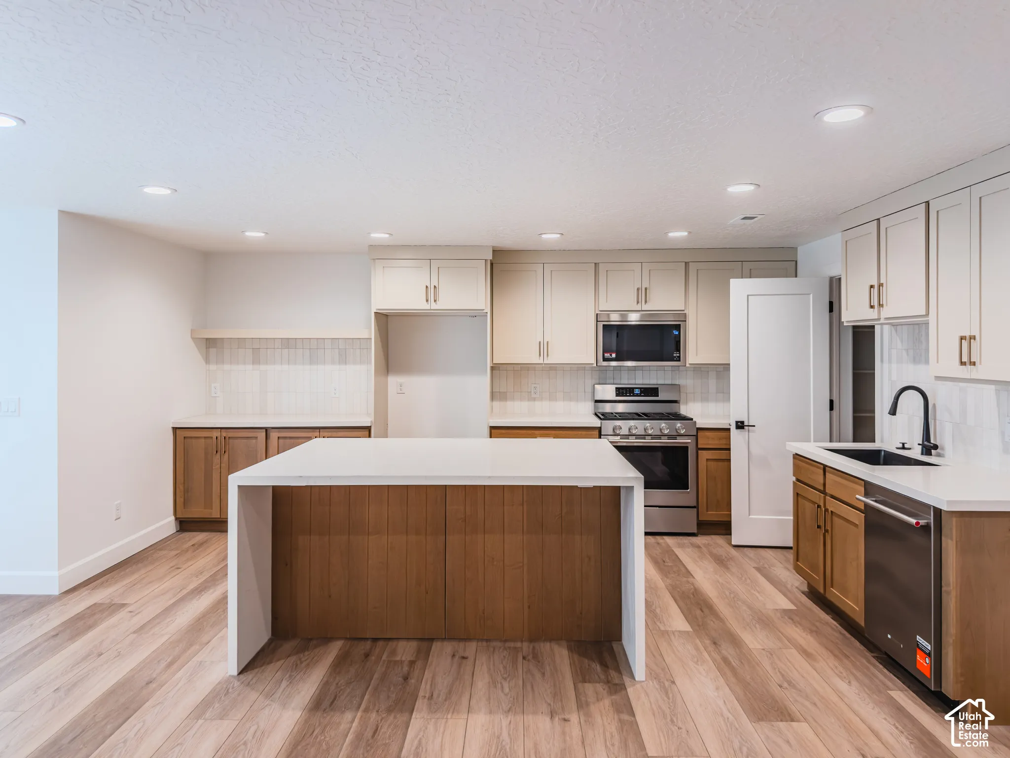 Kitchen featuring a central island with waterfall-edge stone countertop, two-tone cabinetry, recessed lighting, and stainless steel appliances