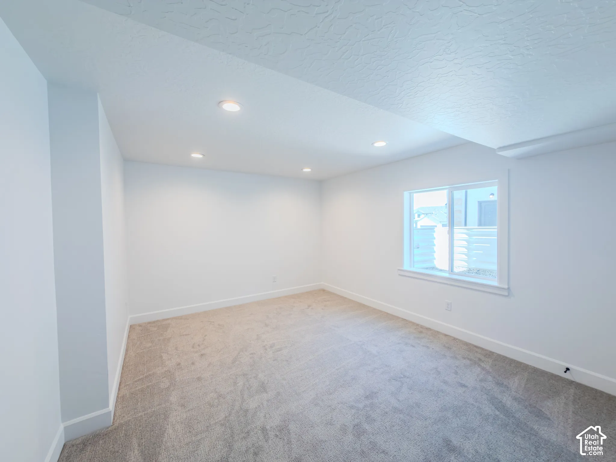 Neutral-toned interior space featuring wall-to-wall carpeting, recessed ceiling lighting, and a window with white trim