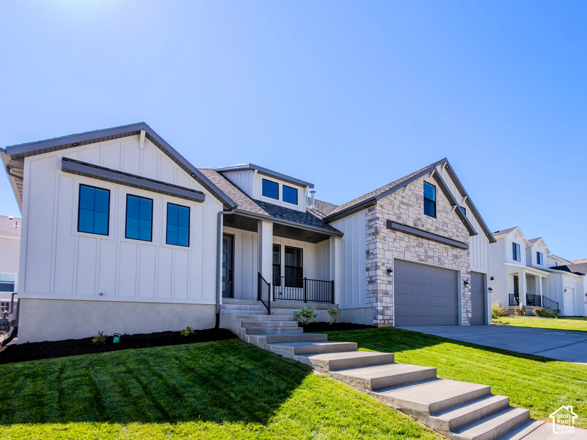 Exterior featuring white vertical siding, stone veneer accents, multi-gabled roofline, concrete stairs, and a three-car garage
