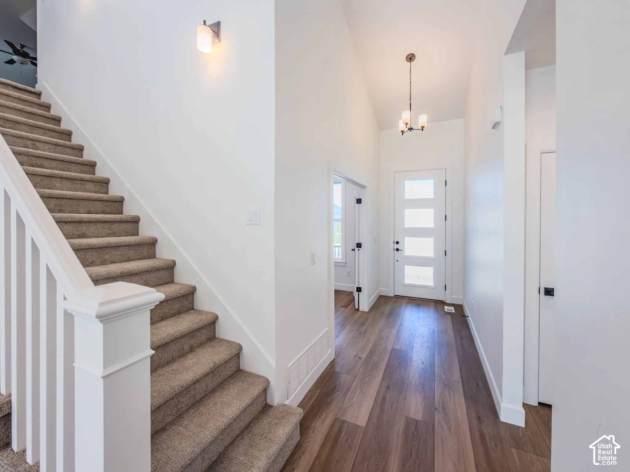 Entryway featuring wood-finish flooring, a staircase with carpeted treads, white-paneled front door with frosted glass inserts, multi-arm chandelier, and a wall-mounted light fixture