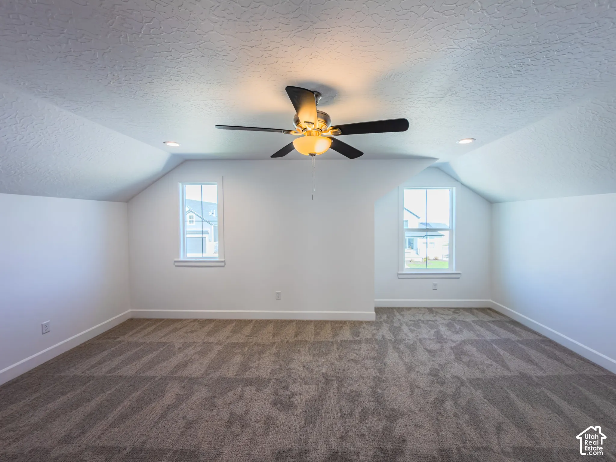 Vaulted ceilings with recessed lighting, wall-to-wall carpeting, and a multi-blade ceiling fan featuring an integrated light fixture, framed by dual windows with muntin detailing
