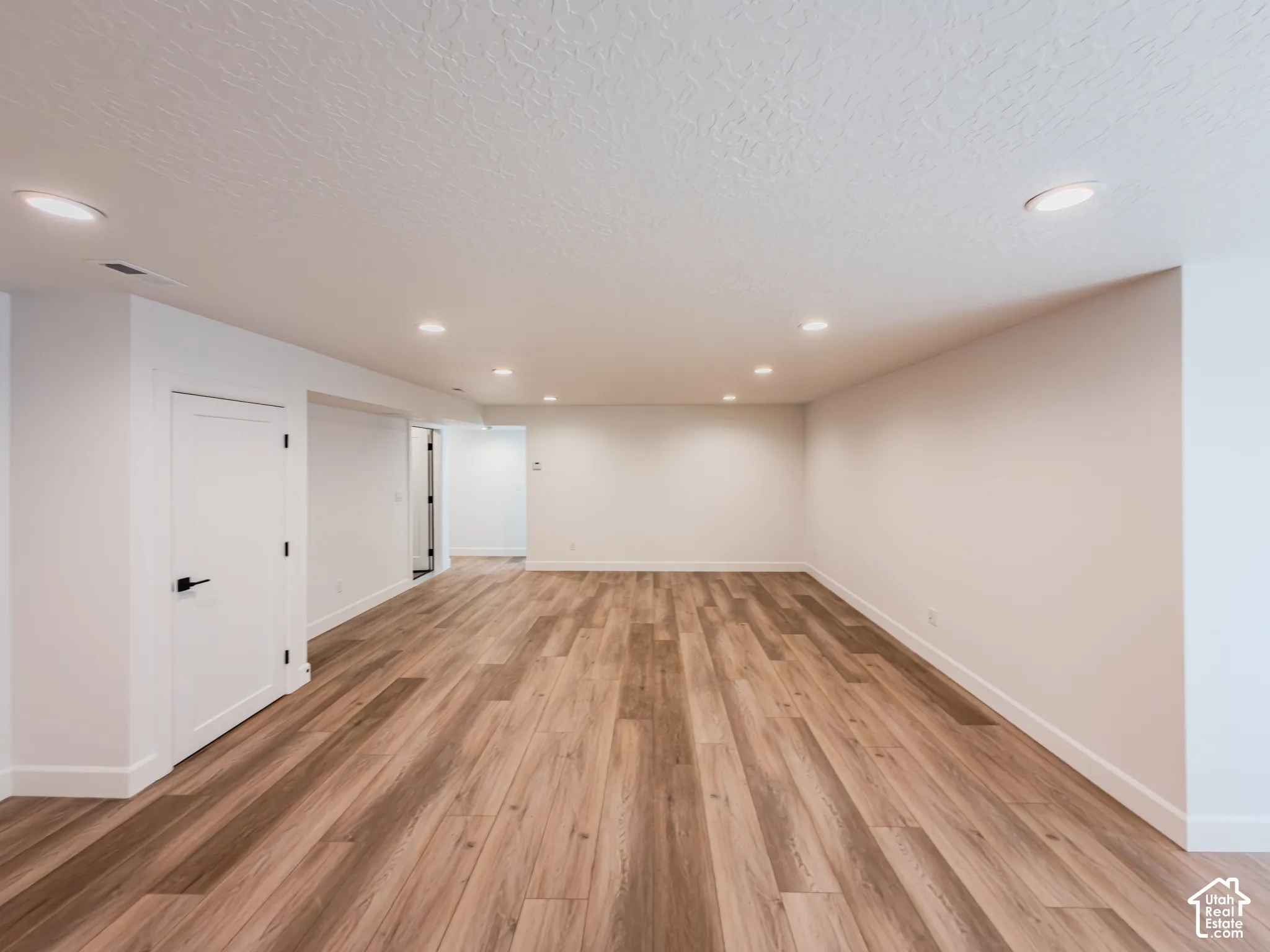Open-concept interior featuring wood-finish flooring, recessed lighting, and crisp white interior doors with matte black hardware