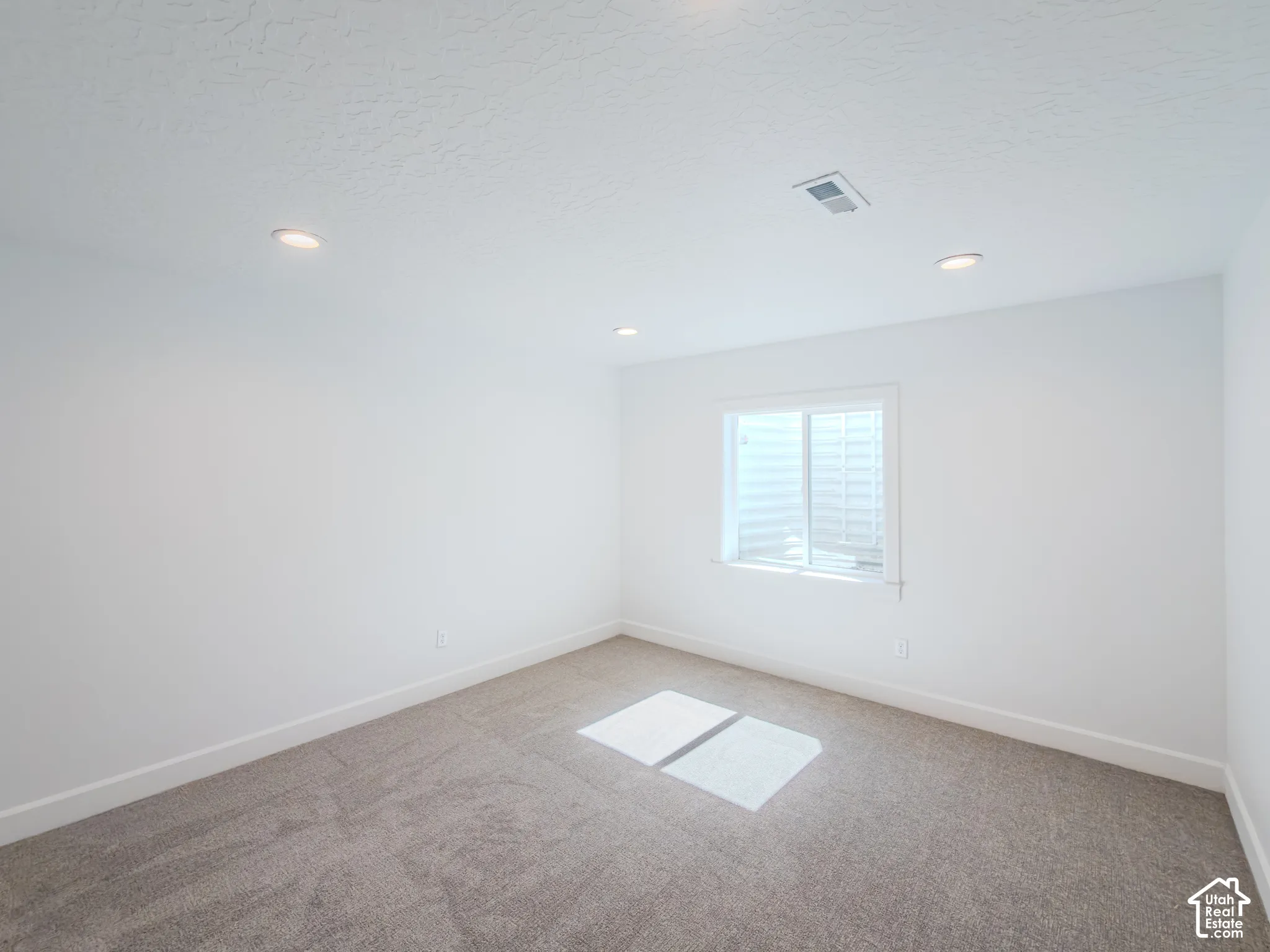 Neutral-toned room featuring high-pile wall-to-wall carpeting, recessed ceiling lighting, and a window with a window well