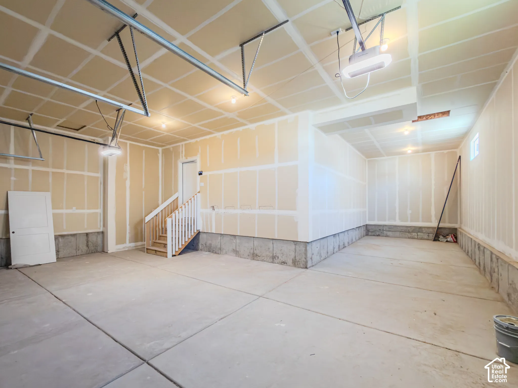 Multi-car garage featuring expansive concrete flooring, unfinished drywall, overhead lighting, and an internal wooden staircase with balustrades