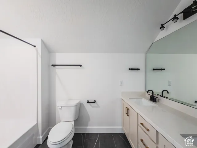 Vanity with stone countertop, dual undermount sinks, matte black fixtures, and large wall-mounted mirror, featuring dark tiled flooring and a shower-tub combination
